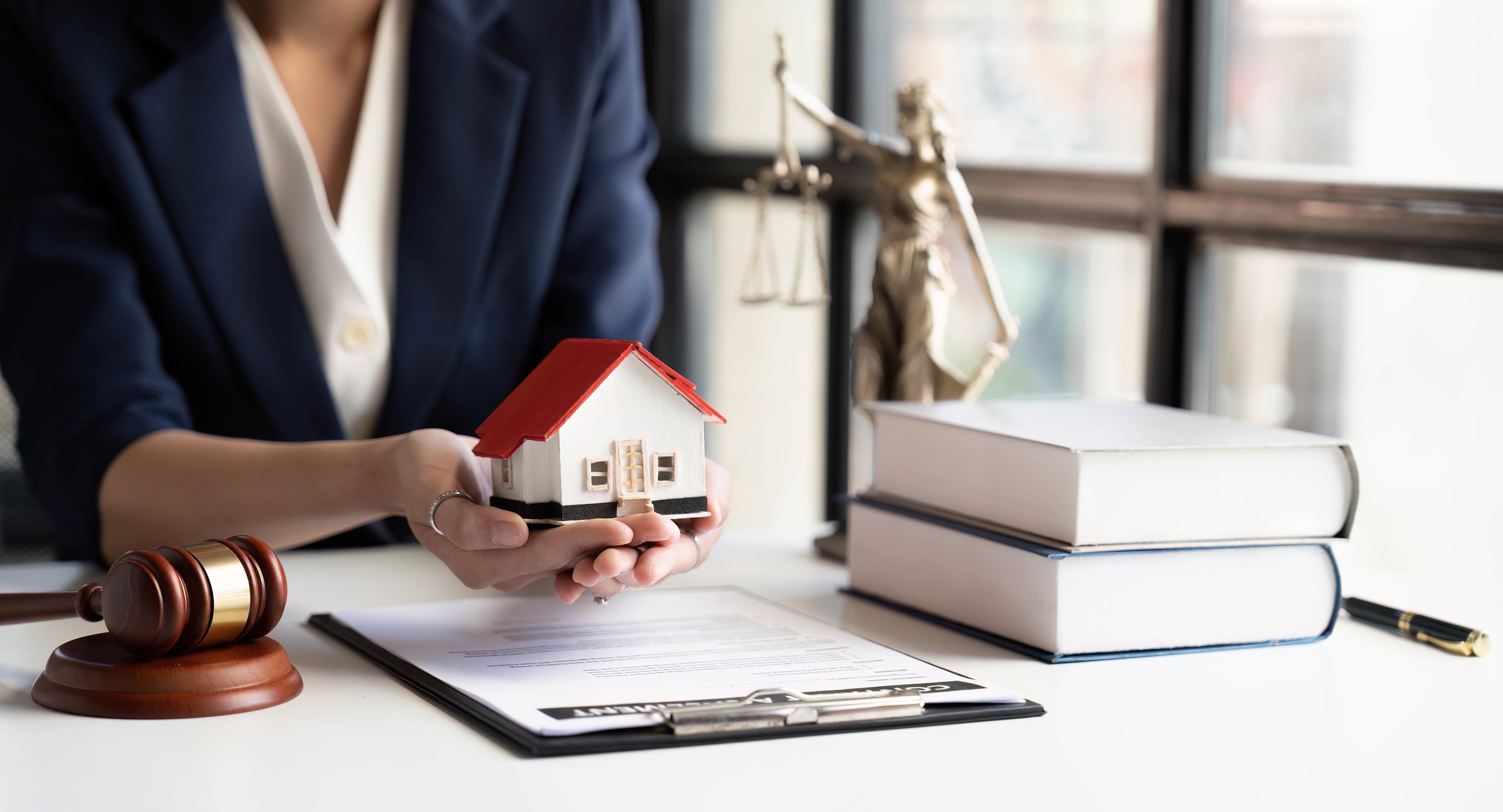 roperty lawyer holding a small house model over legal documents with gavel, law books, and Lady Justice statue in the background, property law and conveyancing.