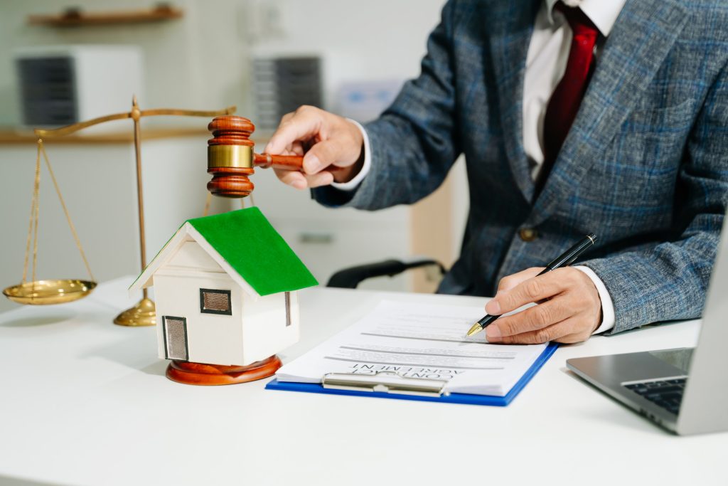 Lawyer in a suit reviewing a property contract at a desk, and a small house model symbolising property law.
