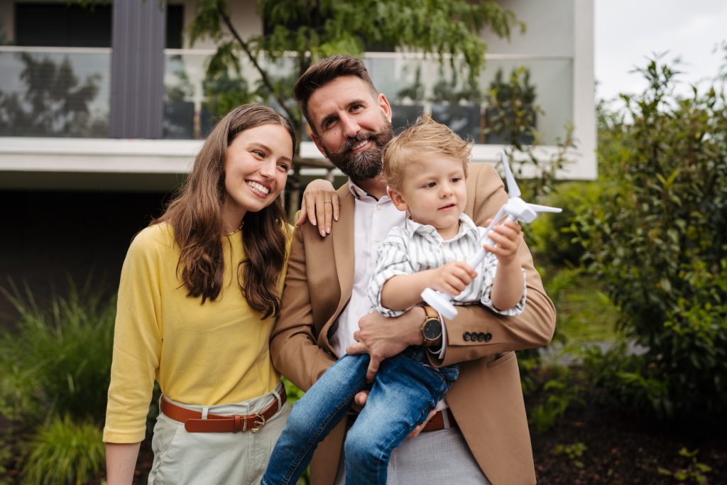 Smiling parents with little son blowing on wind turbine model