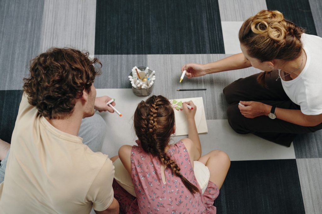 Parents and a child sitting on the floor drawing together, representing family support and child focused decision making